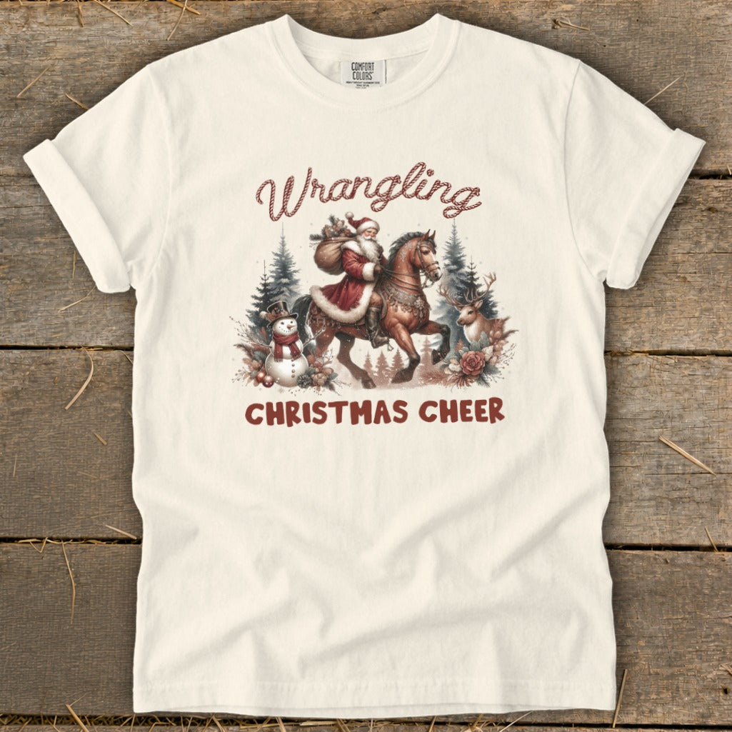 Cream t-shirt with Santa on horseback, snowman, and deer. Text reads "Wrangling Christmas Cheer".
