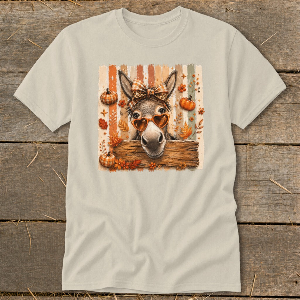 Donkey wearing heart sunglasses and a bow behind a wooden fence with pumpkins and fall leaves.