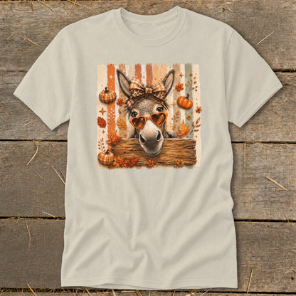 Donkey wearing heart sunglasses and a bow behind a wooden fence with pumpkins and fall leaves.