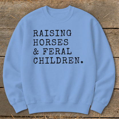 Light blue sweatshirt with black text: "RAISING HORSES & FERAL CHILDREN."