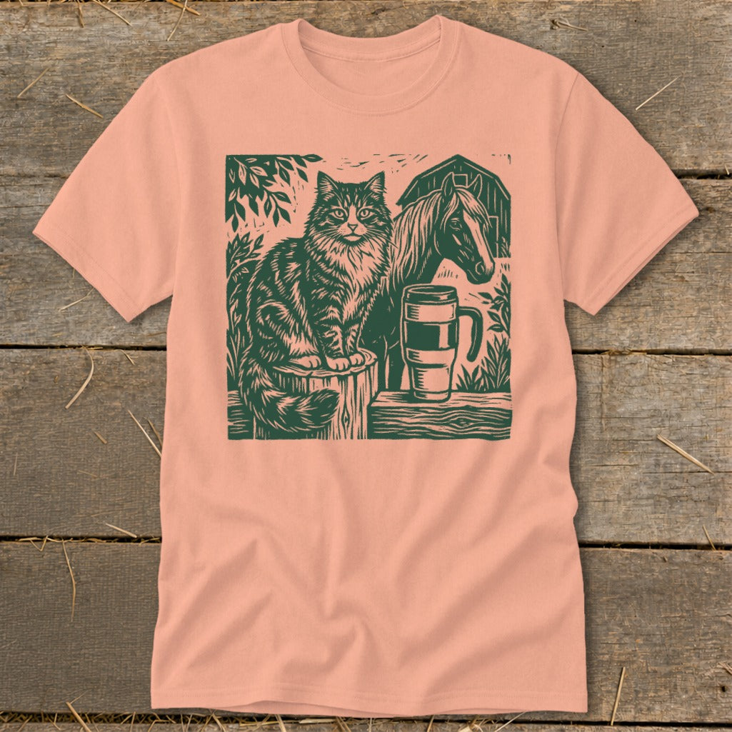 Linocut print of a cat, horse, and mug on a peach t-shirt.