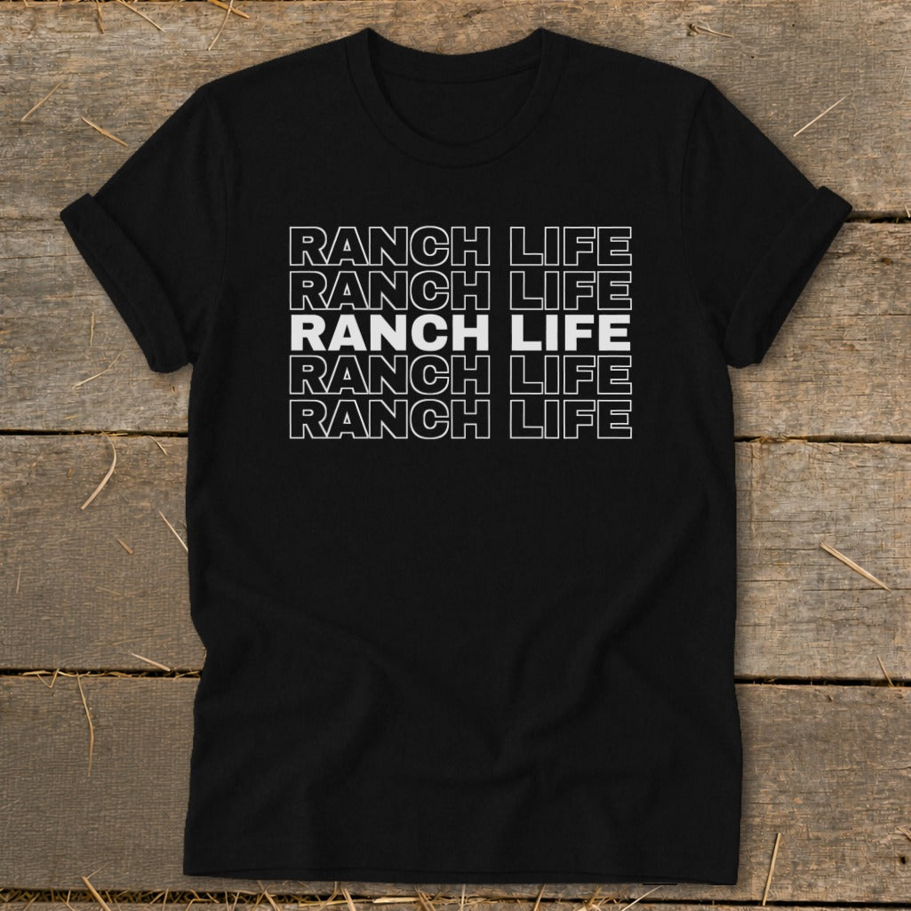 A black t-shirt with rolled sleeves features white stacked text that reads Ranch Life on a wooden background.