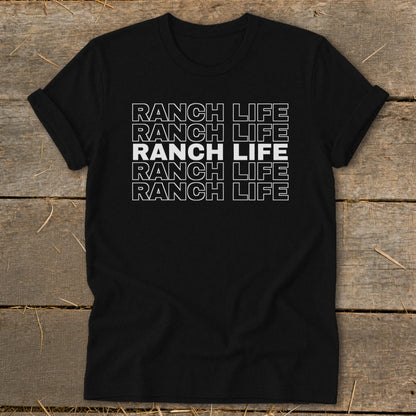 A black t-shirt with rolled sleeves features white stacked text that reads Ranch Life on a wooden background.