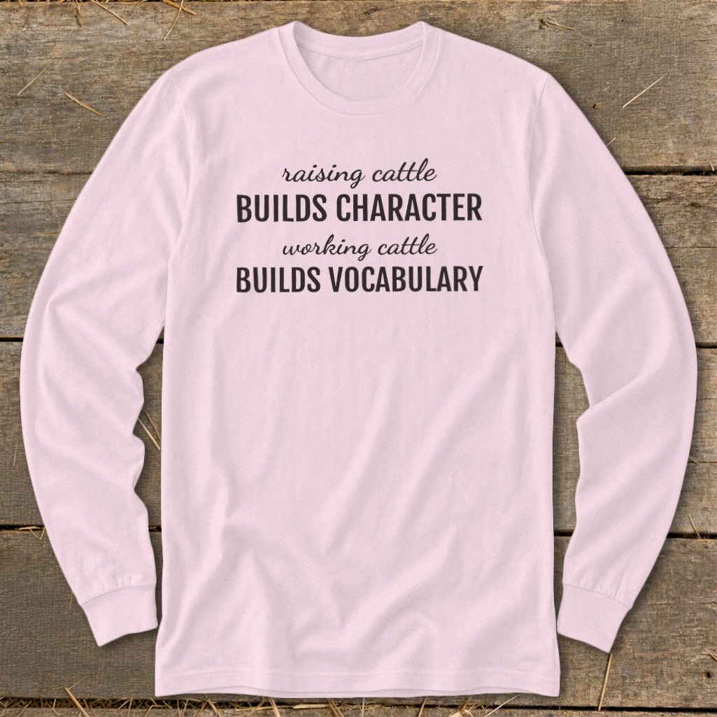 Pink long-sleeve shirt with text: "raising cattle BUILDS CHARACTER working cattle BUILDS VOCABULARY."