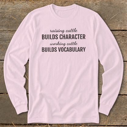 Pink long-sleeve shirt with text: "raising cattle BUILDS CHARACTER working cattle BUILDS VOCABULARY."