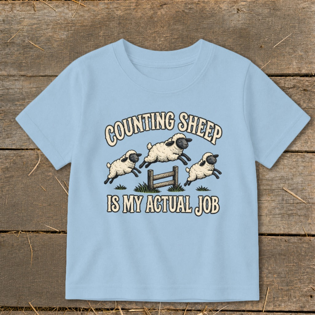 Light blue t-shirt with "COUNTING SHEEP IS MY ACTUAL JOB" and jumping sheep graphic.