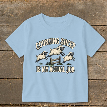 Light blue t-shirt with "COUNTING SHEEP IS MY ACTUAL JOB" and jumping sheep graphic.