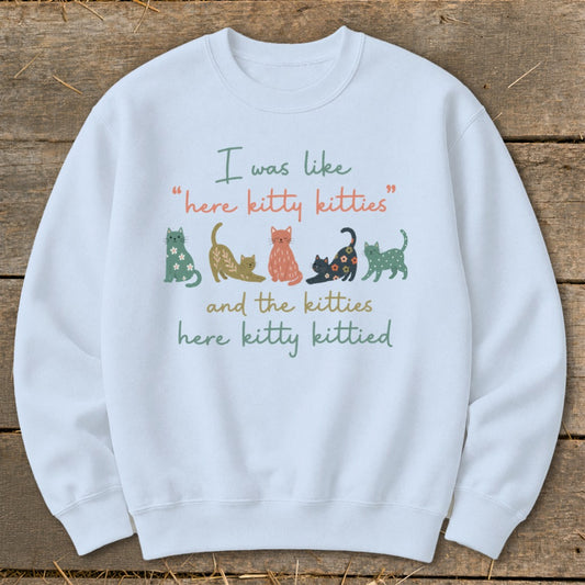 White sweatshirt with graphic of cats and text "I was like 'here kitty kitties' and the kitties here kitty kittied".