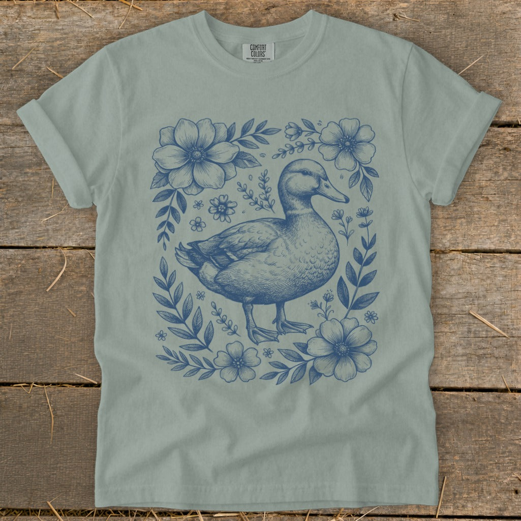 Blue duck and floral illustration on a light green t-shirt.