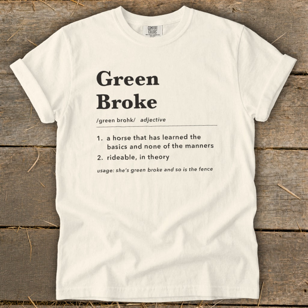 Off-white t-shirt with rolled sleeves laid flat on a rustic wooden background, featuring dictionary-style text defining Green Broke.