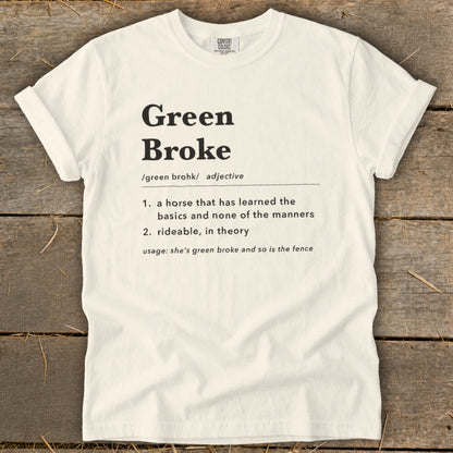 Off-white t-shirt with rolled sleeves laid flat on a rustic wooden background, featuring dictionary-style text defining Green Broke.