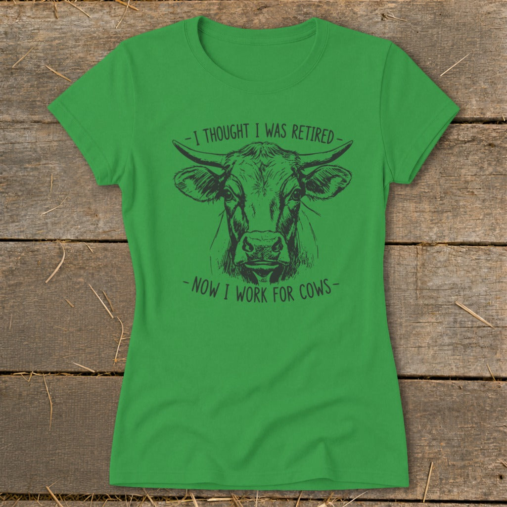 Green t-shirt with a cow illustration and text "I thought I was retired - Now I work for cows".