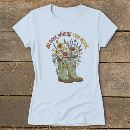 Light blue t-shirt with green boots and flowers graphic reading "Bloom Where You Muck."