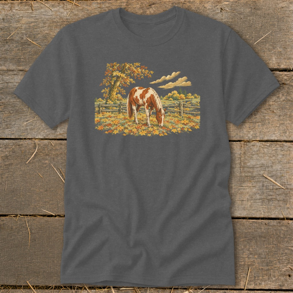 Brown and white horse grazing in a field of autumn leaves with fence and tree.