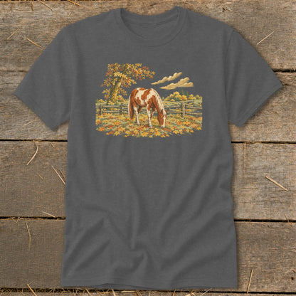 Brown and white horse grazing in a field of autumn leaves with fence and tree.