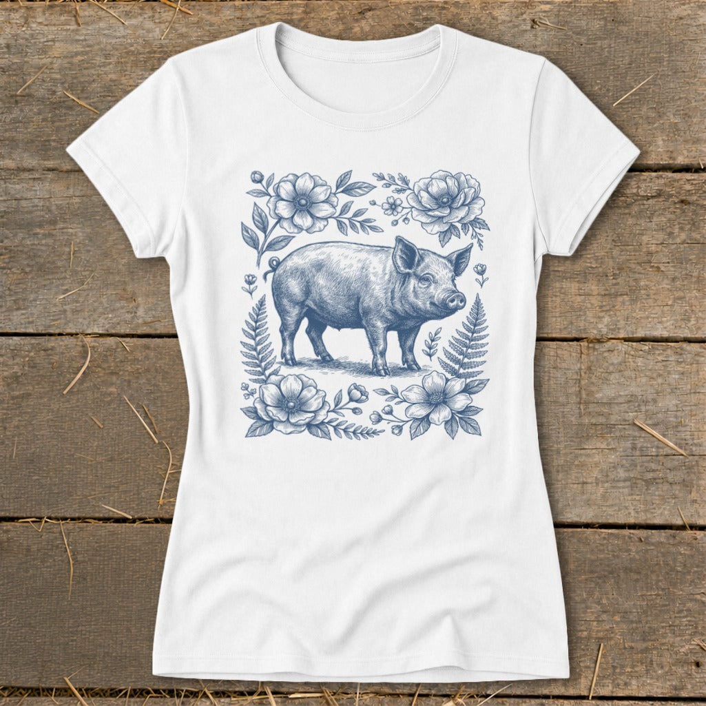 White t-shirt featuring a blue ink drawing of a piglet surrounded by flowers and ferns.
