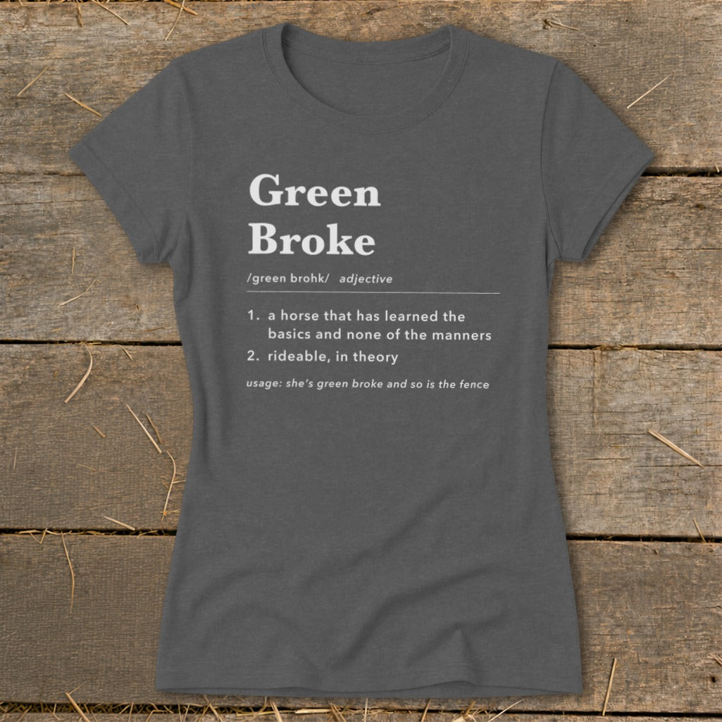 A dark gray women's t-shirt printed with a dictionary-style definition of Green Broke on a rustic wooden background.