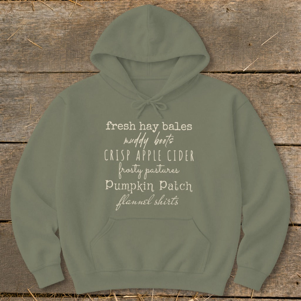 Olive green hoodie with white text: "fresh hay bales, muddy boots, crisp apple cider, frosty pastures, Pumpkin Patch, flannel shirts."