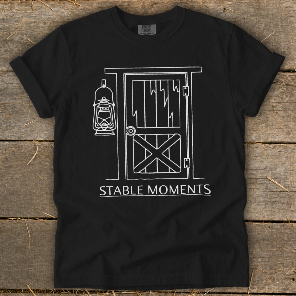 Black t-shirt with white line art of a barn door and lantern, text "STABLE MOMENTS".