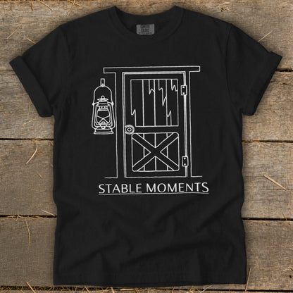 Black t-shirt with white line art of a barn door and lantern, text "STABLE MOMENTS".