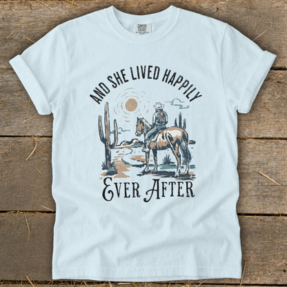 T-shirt with desert scene: woman on horse, cacti, and text "And She Lived Happily Ever After".