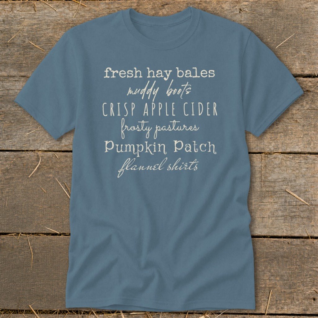 Blue t-shirt with white text listing fall activities: fresh hay bales, muddy boots, crisp apple cider, frosty pastures, pumpkin patch, flannel shirts.
