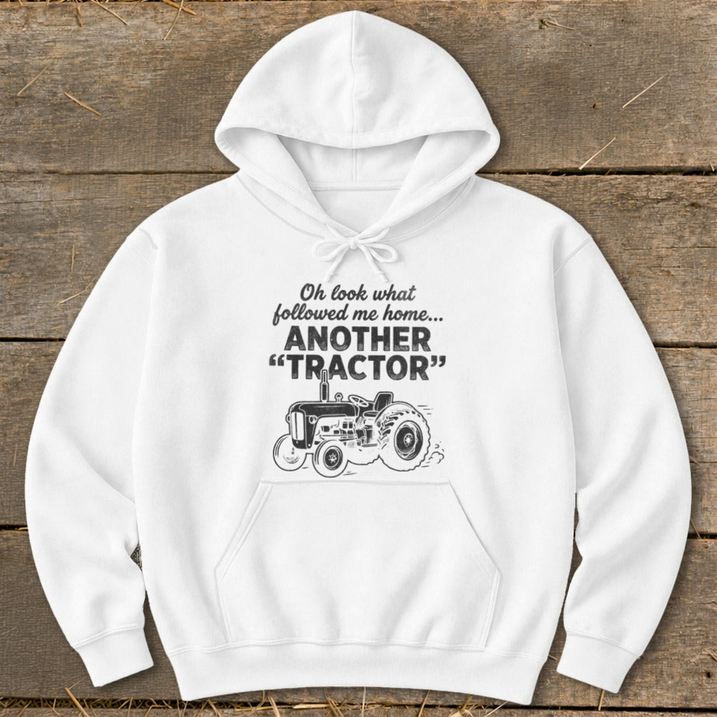 White hoodie with graphic text "Oh look what followed me home... ANOTHER "TRACTOR"" and a tractor illustration.