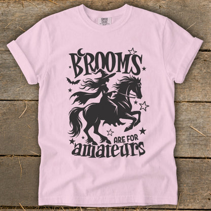 Pink t-shirt with black graphic of witch on a horse and text "Brooms are for amateurs".