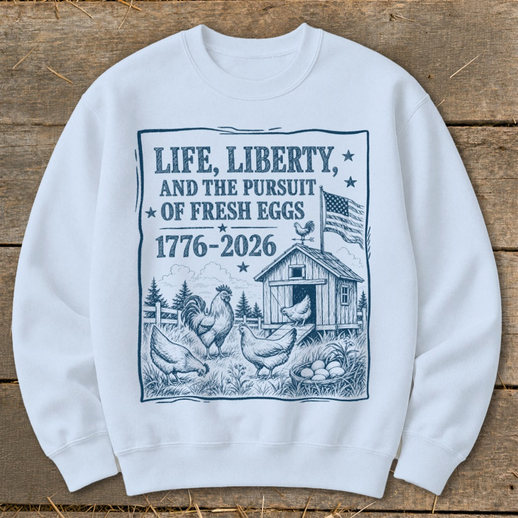 White sweatshirt with print: "Life, Liberty, and the Pursuit of Fresh Eggs 1776-2026", chickens, and barn.