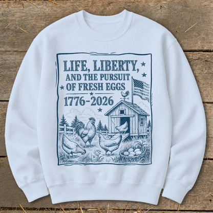 White sweatshirt with print: "Life, Liberty, and the Pursuit of Fresh Eggs 1776-2026", chickens, and barn.