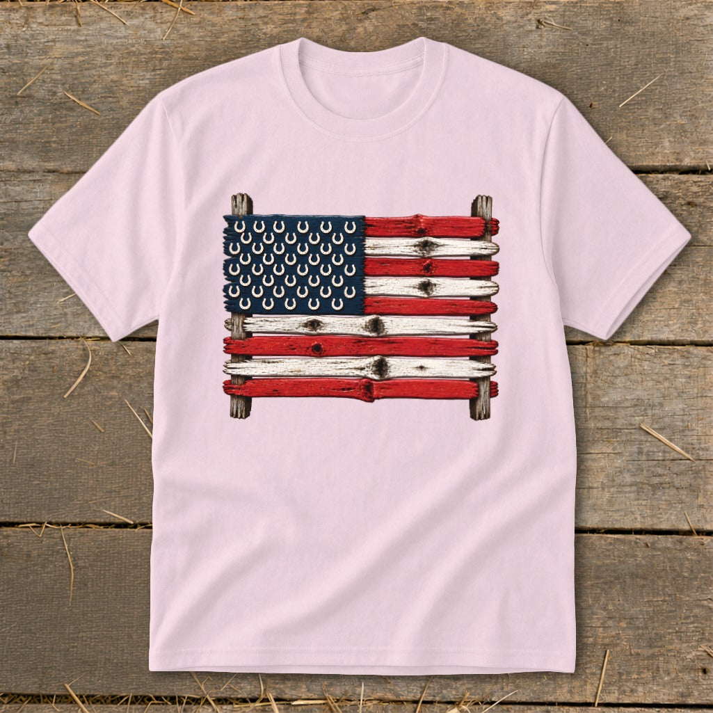 Light pink t-shirt featuring an American flag made of painted wooden planks and horseshoes on a rustic wooden background.