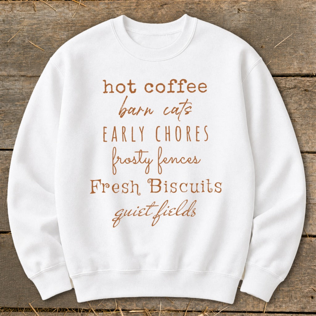 White sweatshirt with brown text: hot coffee, barn cats, early chores, frosty fences, fresh biscuits, quiet fields.