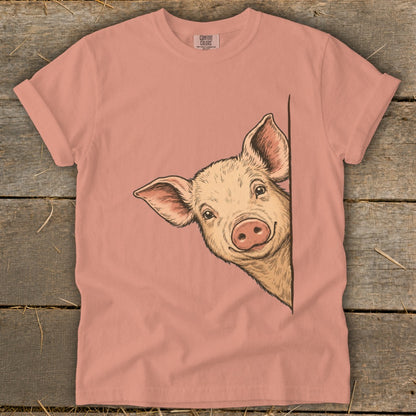 Pink t-shirt with a hand-drawn illustration of a smiling pig peeking from the side.