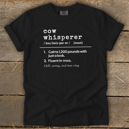 Black t-shirt with white text defining "cow whisperer" with humorous descriptions.