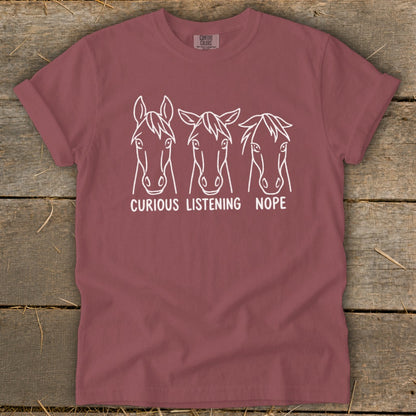 Mauve short-sleeve t-shirt featuring a white line graphic of three horses with the text curious listening nope.
