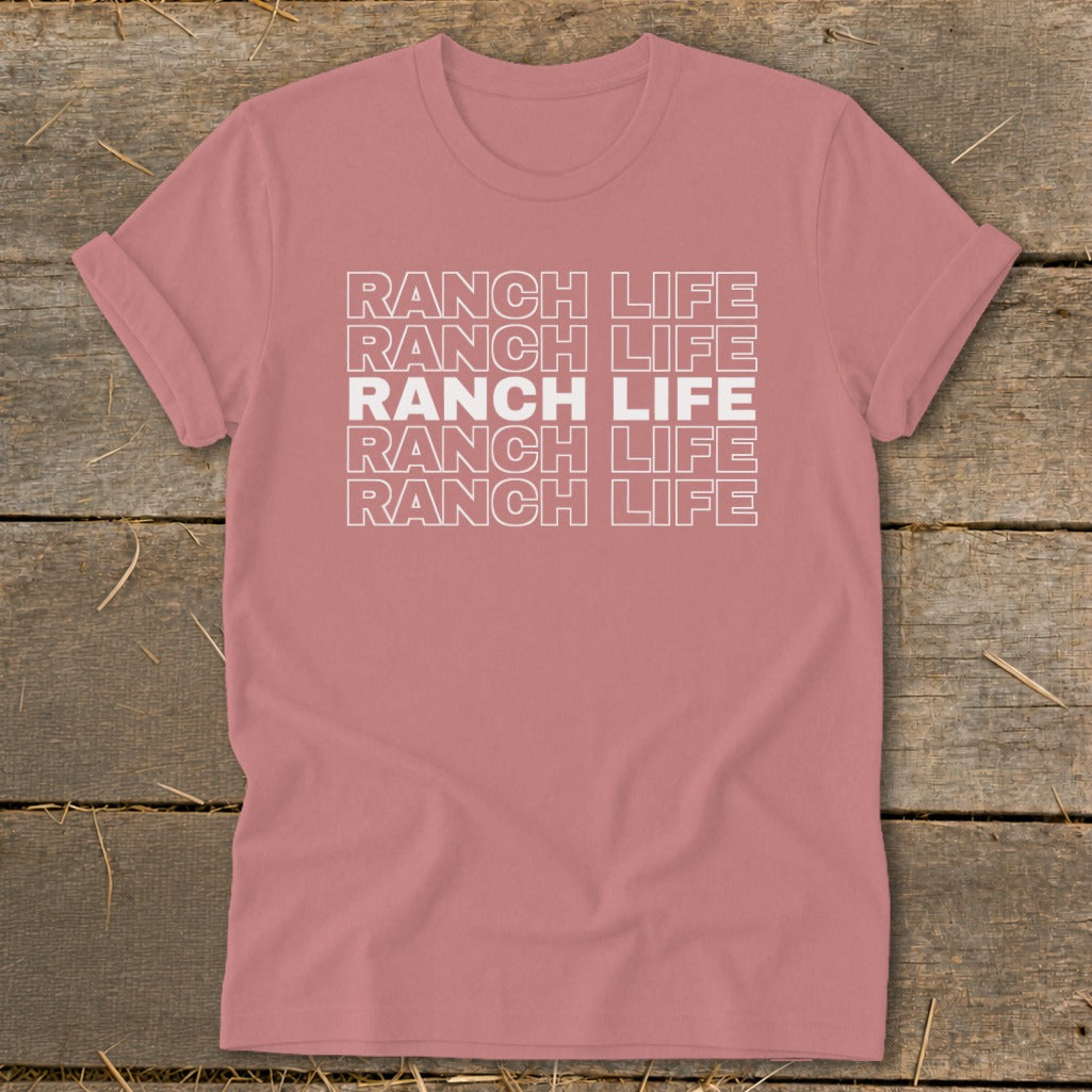 A mauve t-shirt featuring the stacked white text RANCH LIFE lies flat on a wooden surface.