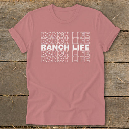 A mauve t-shirt featuring the stacked white text RANCH LIFE lies flat on a wooden surface.