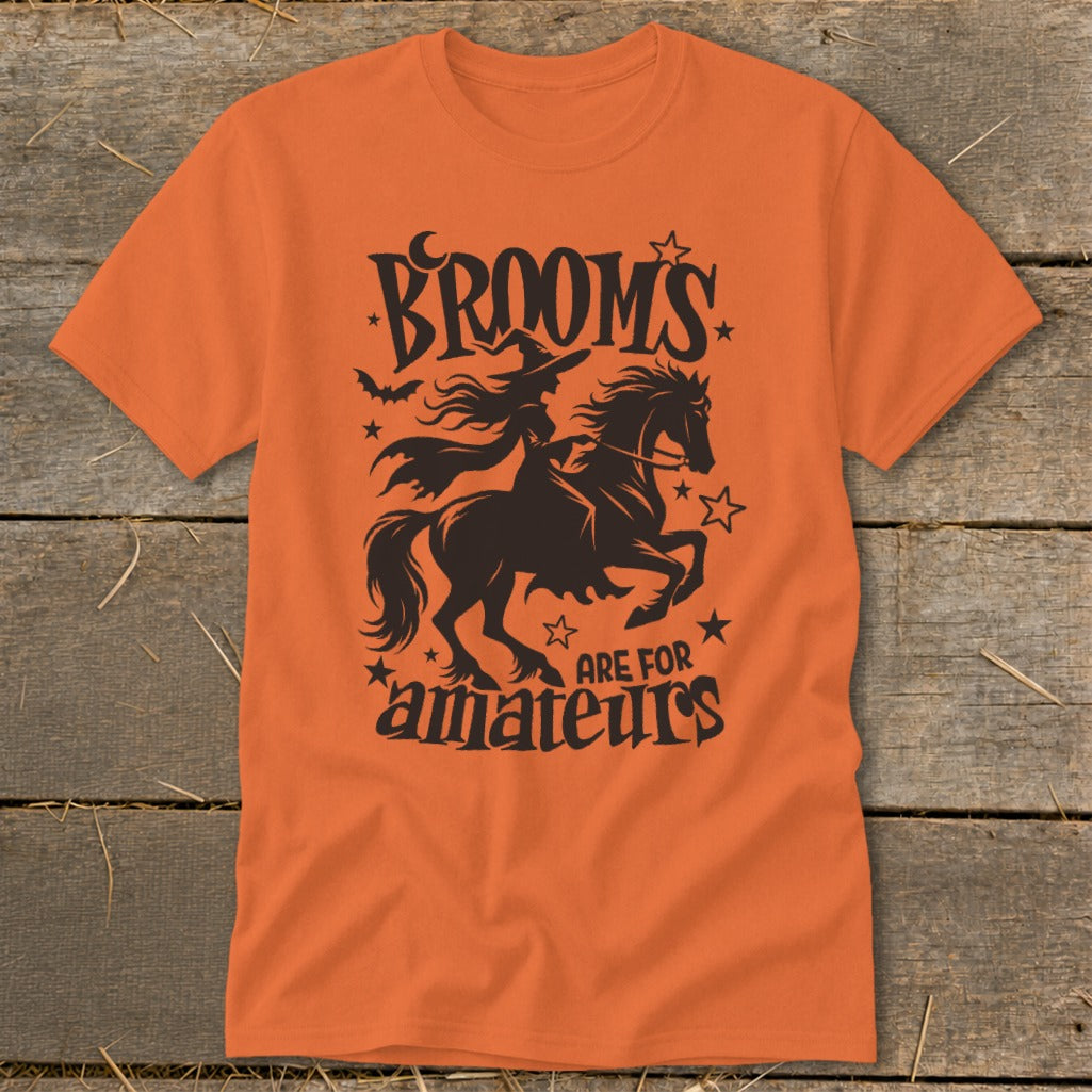 Orange t-shirt with black Halloween graphic of witch on horse, text "BROOMS ARE FOR amateurs".