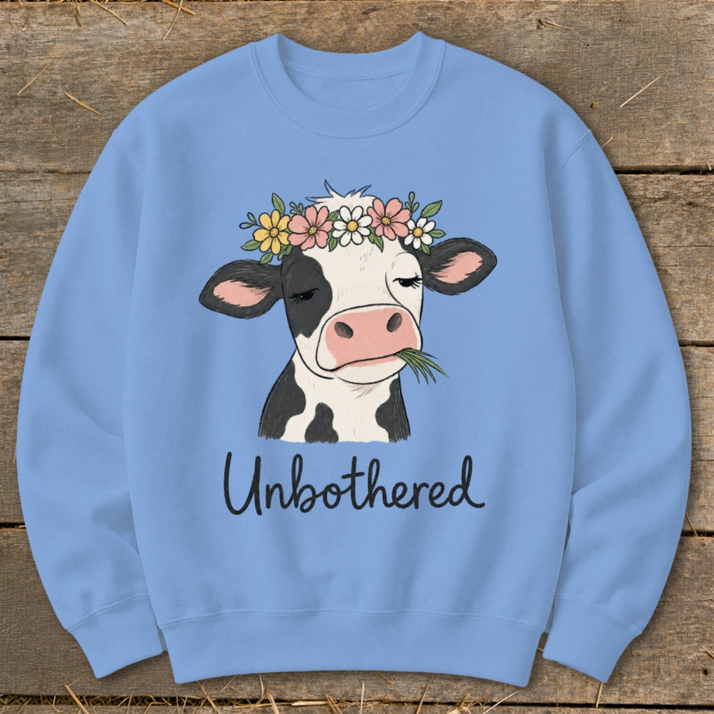 Light blue sweatshirt with black and white cow wearing a flower crown, eating grass.