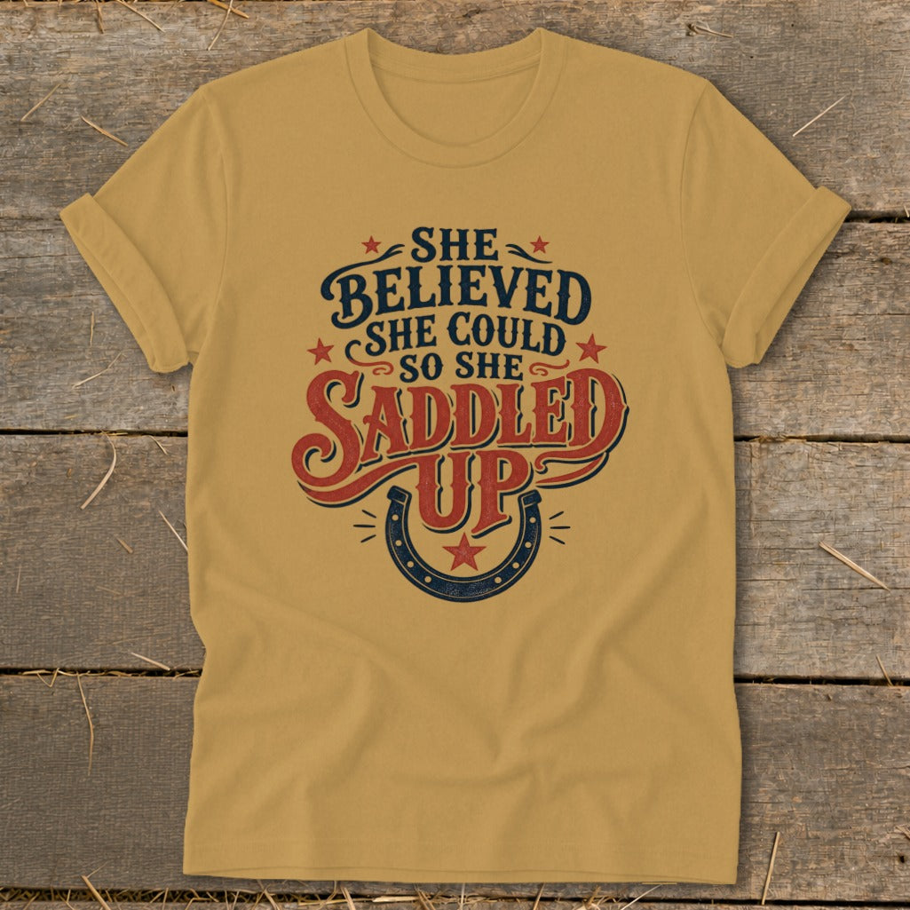 Gold t-shirt with "She Believed She Could So She Saddled Up" text and horseshoe.