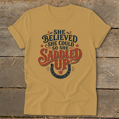 Gold t-shirt with "She Believed She Could So She Saddled Up" text and horseshoe.