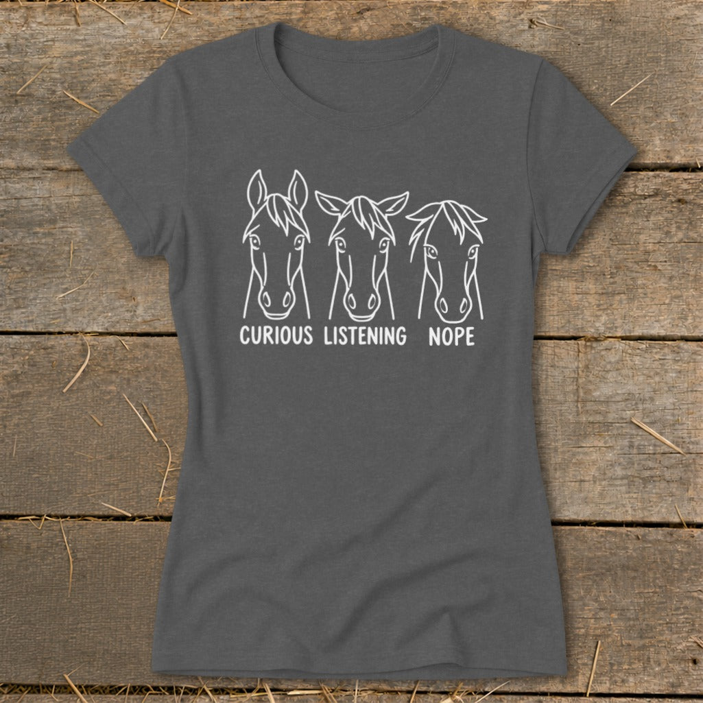 A dark gray short-sleeved t-shirt features three line-drawn horse heads with the captions "CURIOUS," "LISTENING," and "NOPE."
