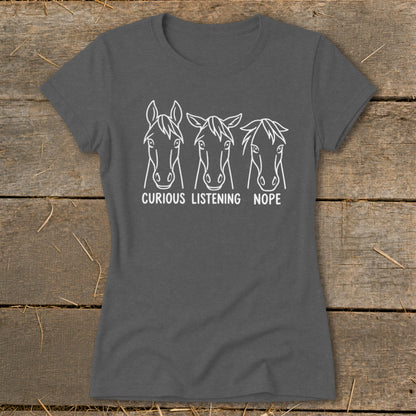 A dark gray short-sleeved t-shirt features three line-drawn horse heads with the captions "CURIOUS," "LISTENING," and "NOPE."