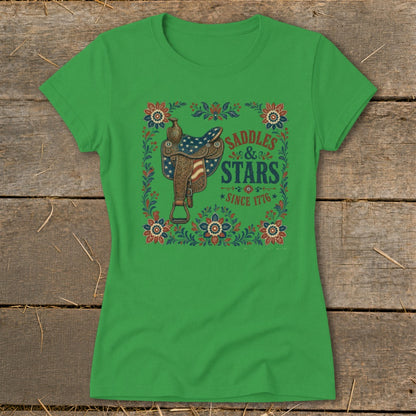 Green t-shirt with a saddle design featuring American flag elements and text "SADDLES & STARS SINCE 1776".