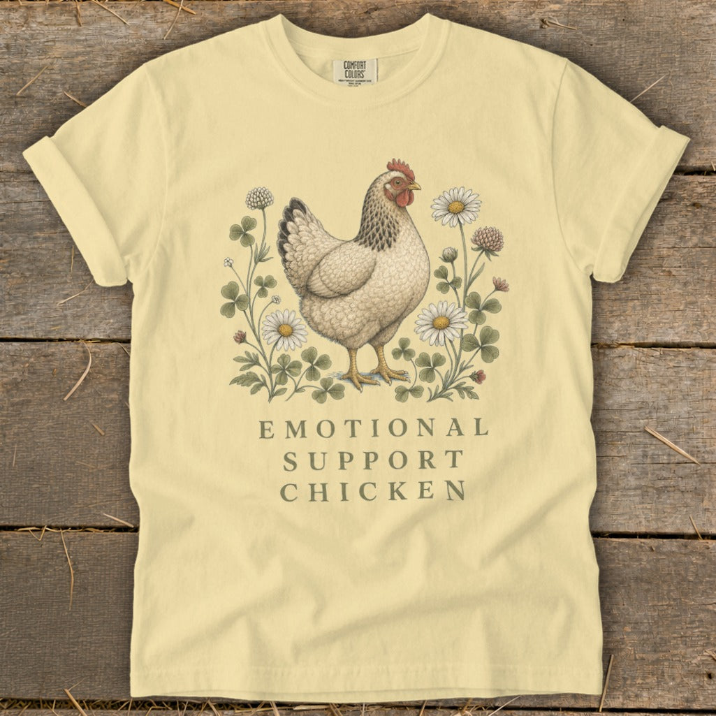Pale yellow t-shirt with hen illustration and "Emotional Support Chicken" text.
