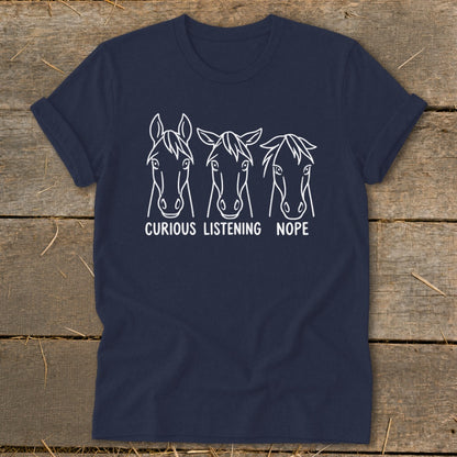 Dark blue t-shirt featuring a white line art graphic of three horse heads with the text "CURIOUS," "LISTENING," and "NOPE."