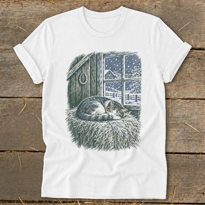 T-shirt with a drawing of a cat sleeping on hay by a snowy window.