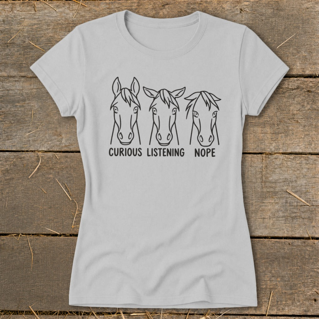 A light gray women's t-shirt features three line-drawn horse heads with the text "CURIOUS LISTENING NOPE" underneath.