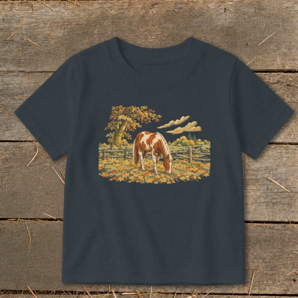 Brown and white horse grazing in a field of autumn leaves.
