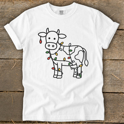 White t-shirt with a line drawing of a cow decorated with colorful Christmas lights.